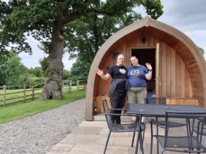 Dan and Ruth outside a wooden "pod" glamping structure.