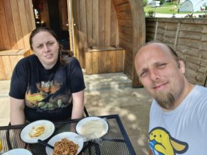 Ruth and Dan eat (fake) duck pancakes outside their lodge.