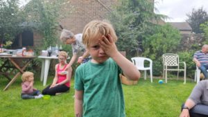 A child in the smoke of a barbecue holds his hand over his eyes.