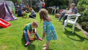 Children play together; adults sit and talk in the background.