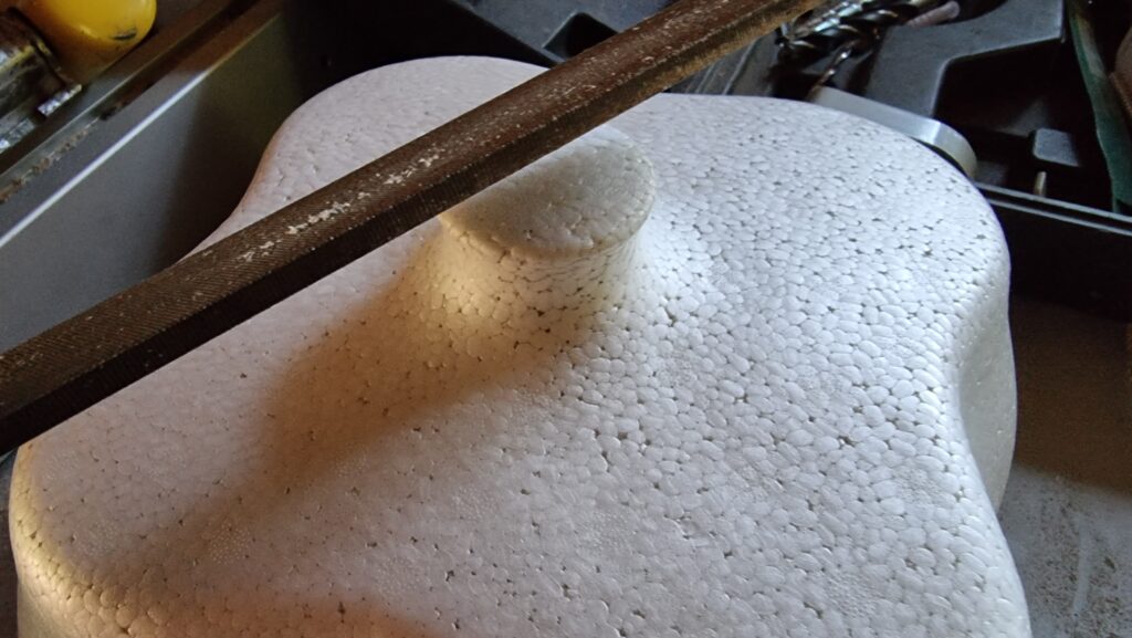 Top of a reinforced polystyrene doorstep milk storage box, showing the round-topped handle. A metal file sits atop the box, about to be used to file down the handle.