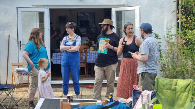 A group of adults stand around on a patio, socialising.