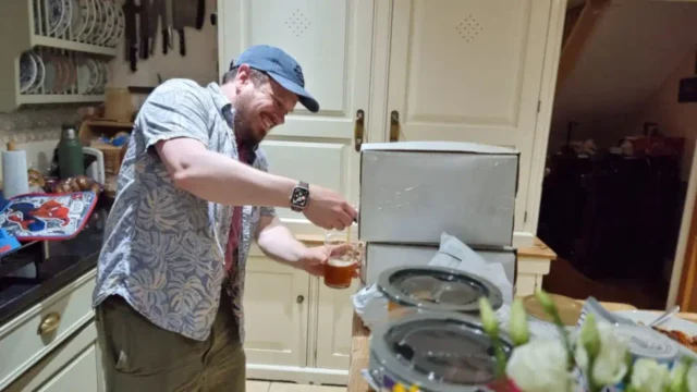 A man wearing a cap pours himself a beer from a 10-litre box.