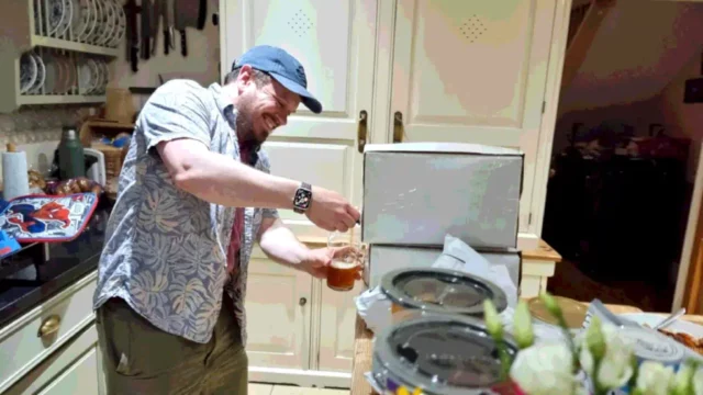 A man wearing a cap pours himself a beer from a 10-litre box, reduced to a "Web safe" palette.