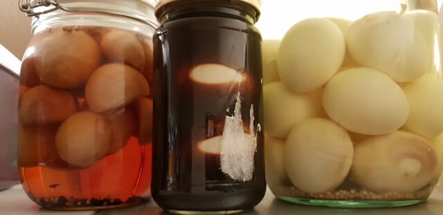 Three jars of homemade pickled eggs; one in each of a chilli-spiced vinegar, balsamic vinegar, and white vinegar.