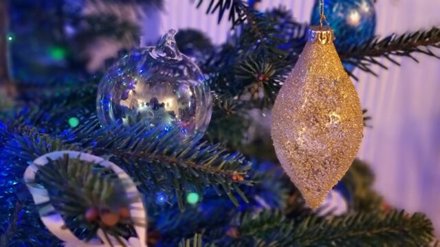 A highly-reflective 'soap bubble' glass bauble hangs alongside a glittery gold teardrop-shaped bauble, lit by green and blue fairy lights.