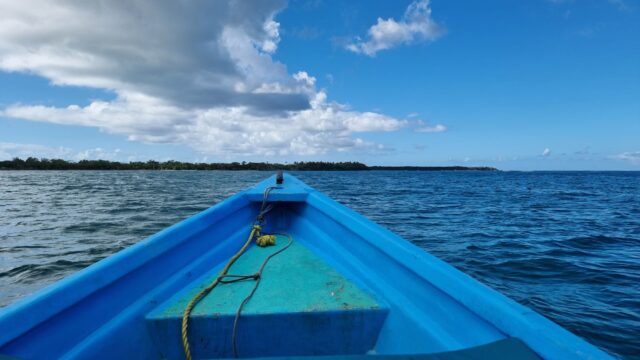 View from the prow of the Cariad, a light blue boat, as she heads towards a distant shore.