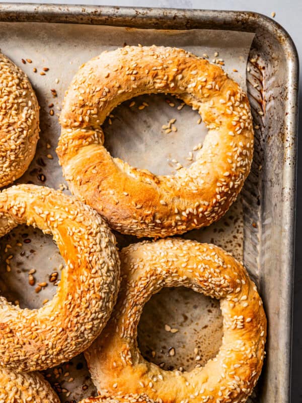 Close-up of baked sesame bagels (Gevrek) on a lined baking sheet.