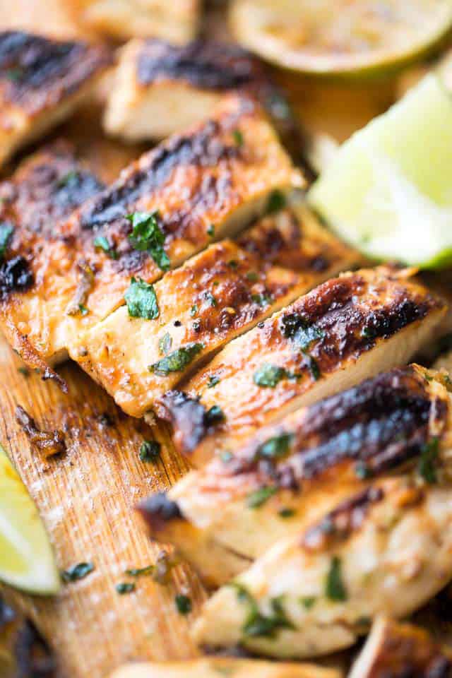 Lime marinated roasted chicken breast cut into slices on a wooden cutting board.