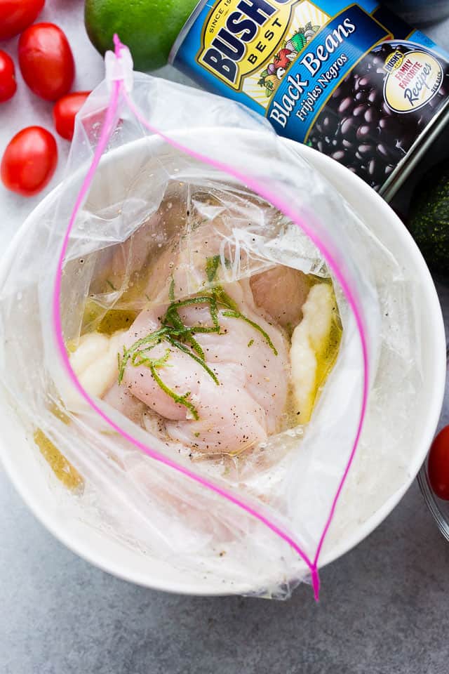 Overhead view of chicken combined with lime marinade in a Ziploc bag set inside a bowl.