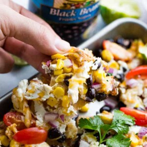 A hand lifting a tortilla chip from a pan of chicken nachos.