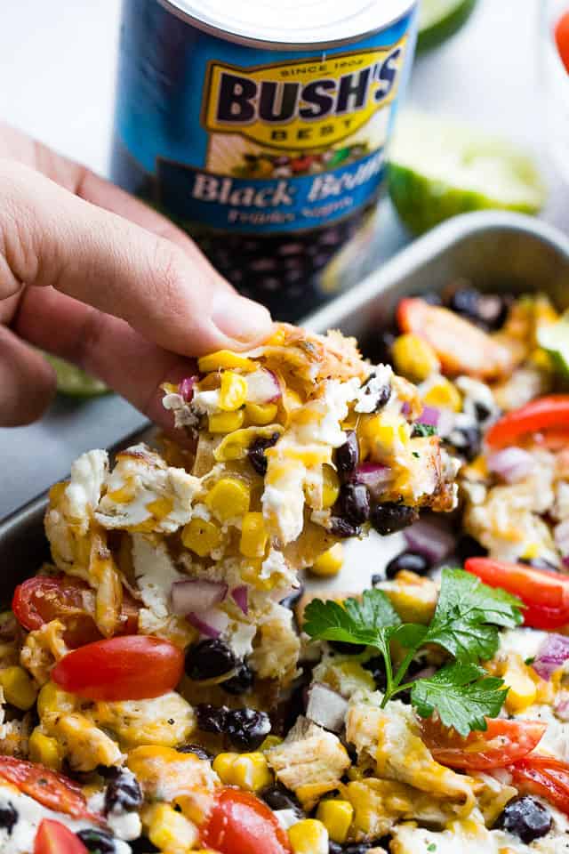 A hand lifting a tortilla chip from a pan of chicken nachos.