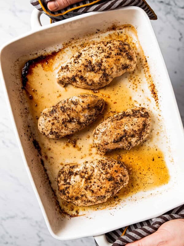 Hands holding baked chicken breasts in baking dish