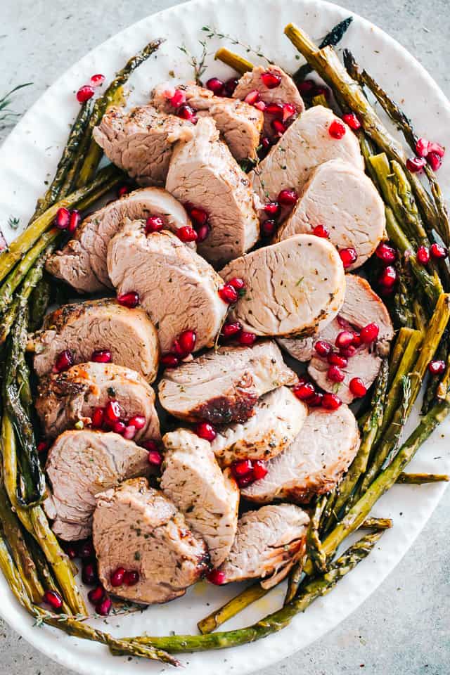 An oval-shaped platter filled with roasted pork tenderloin and roasted asparagus