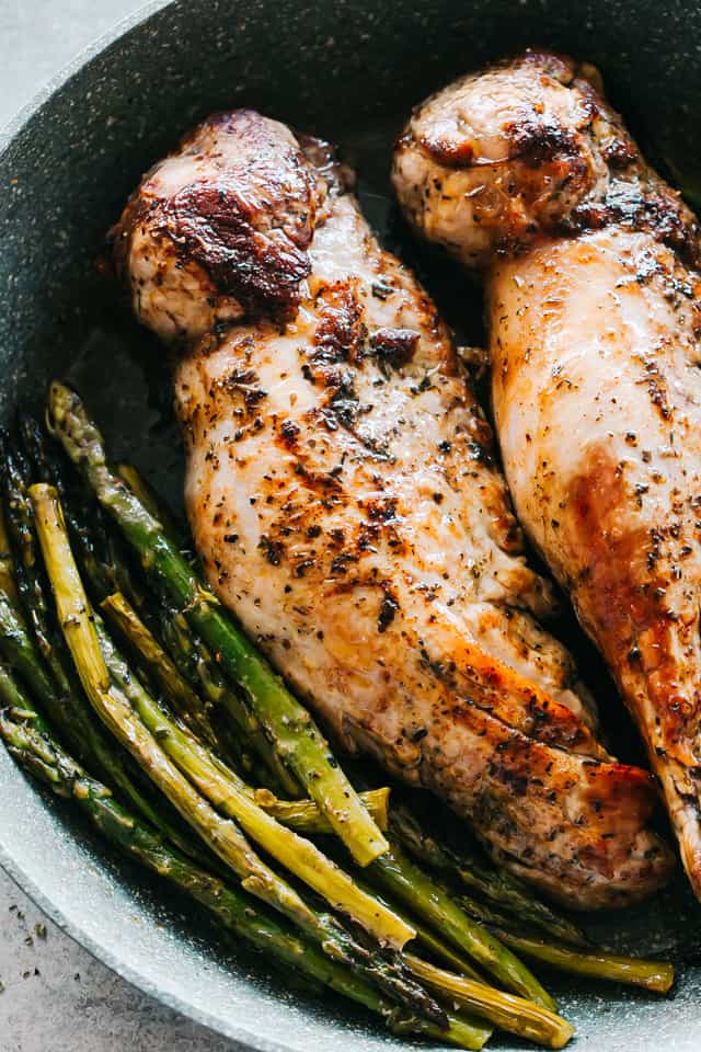 Two whole baked tenderloins in a large skillet with baked asparagus