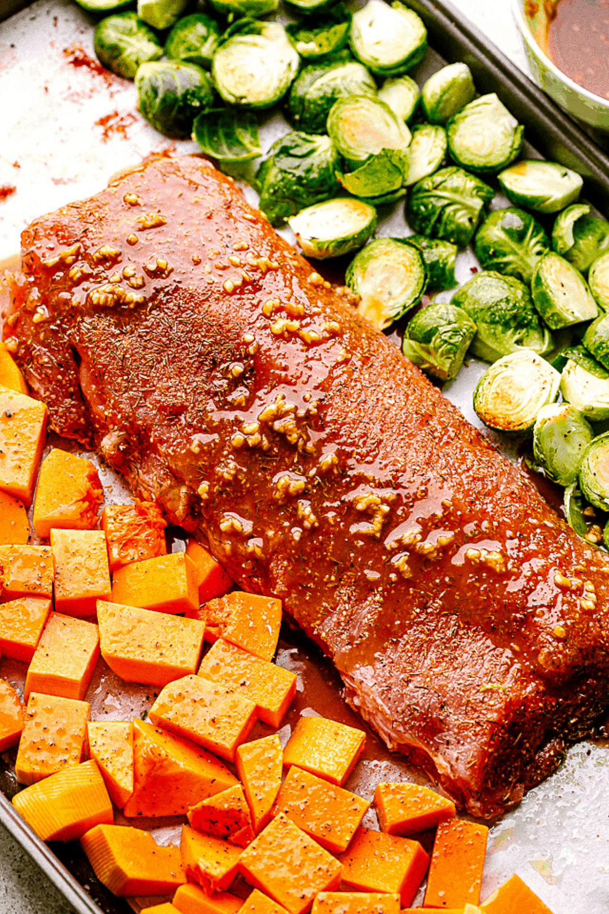 Pork loin on a baking sheet with butternut squash and brussels sprouts, ready to cook. 