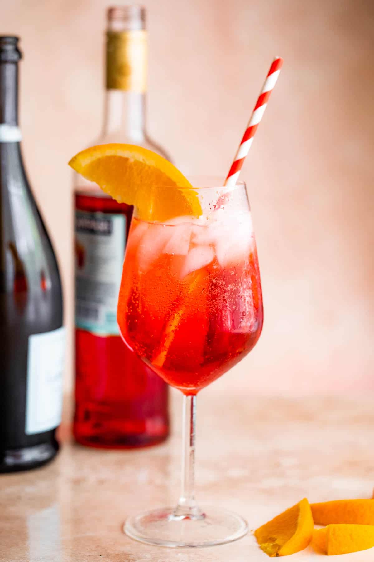 Campari Spritz in a tall stemmed glass served with a slice of orange on the rim and red and white straw