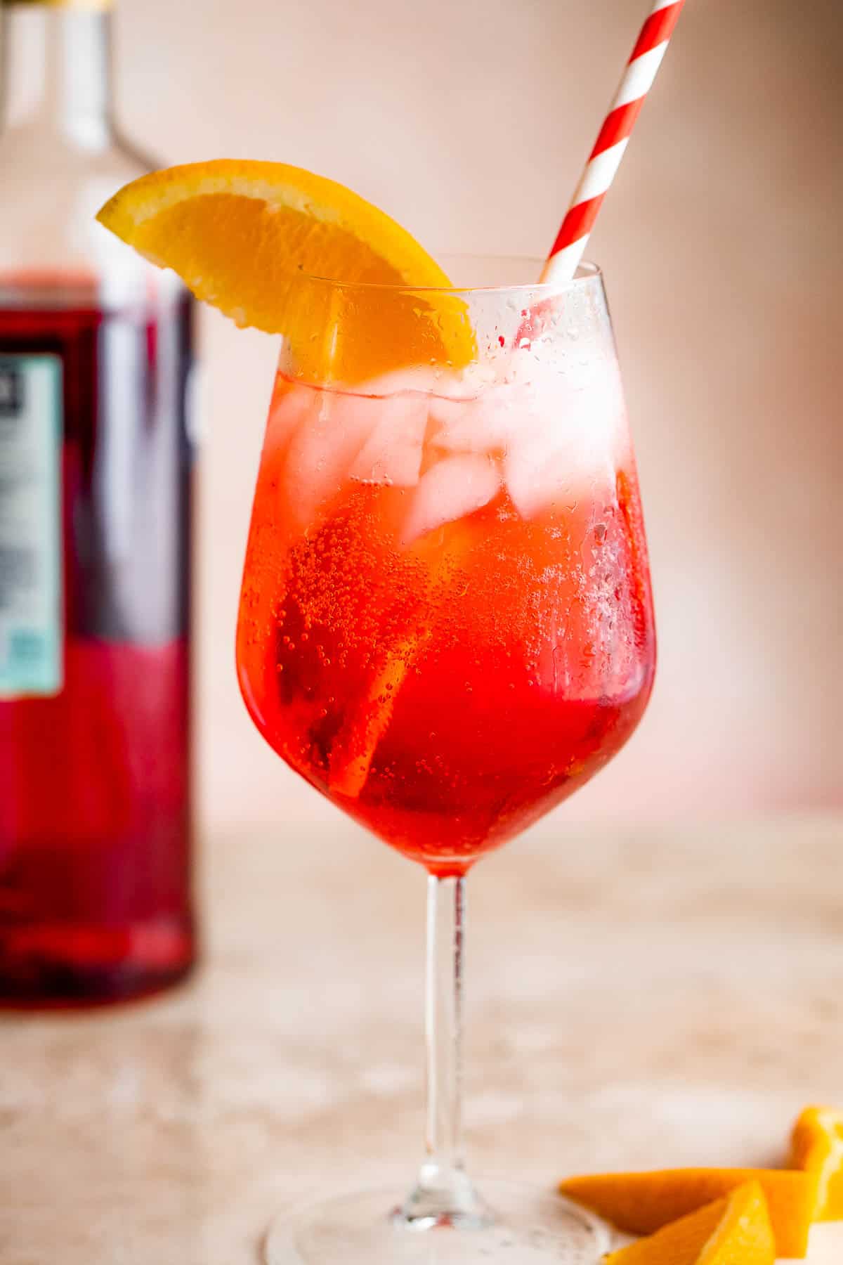 Campari Spritz in a tall stemmed glass served with a slice of orange on the rim and red and white straw