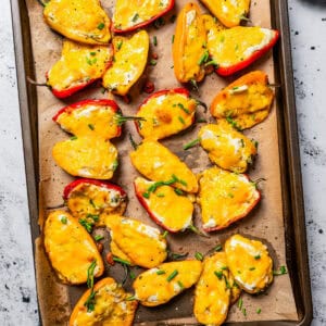 Baked cream cheese stuffed peppers on a lined baking sheet.