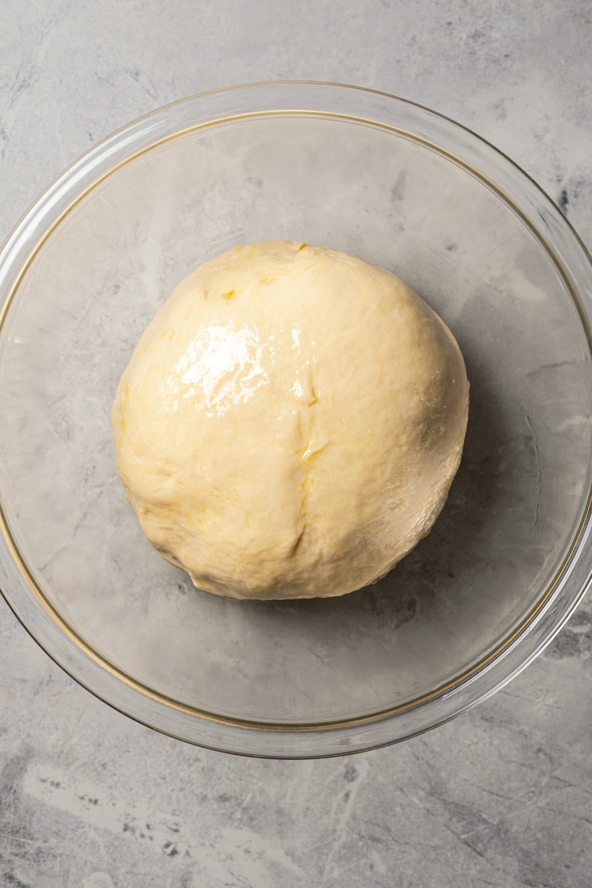 A ball of dinner roll dough inside a glass bowl.