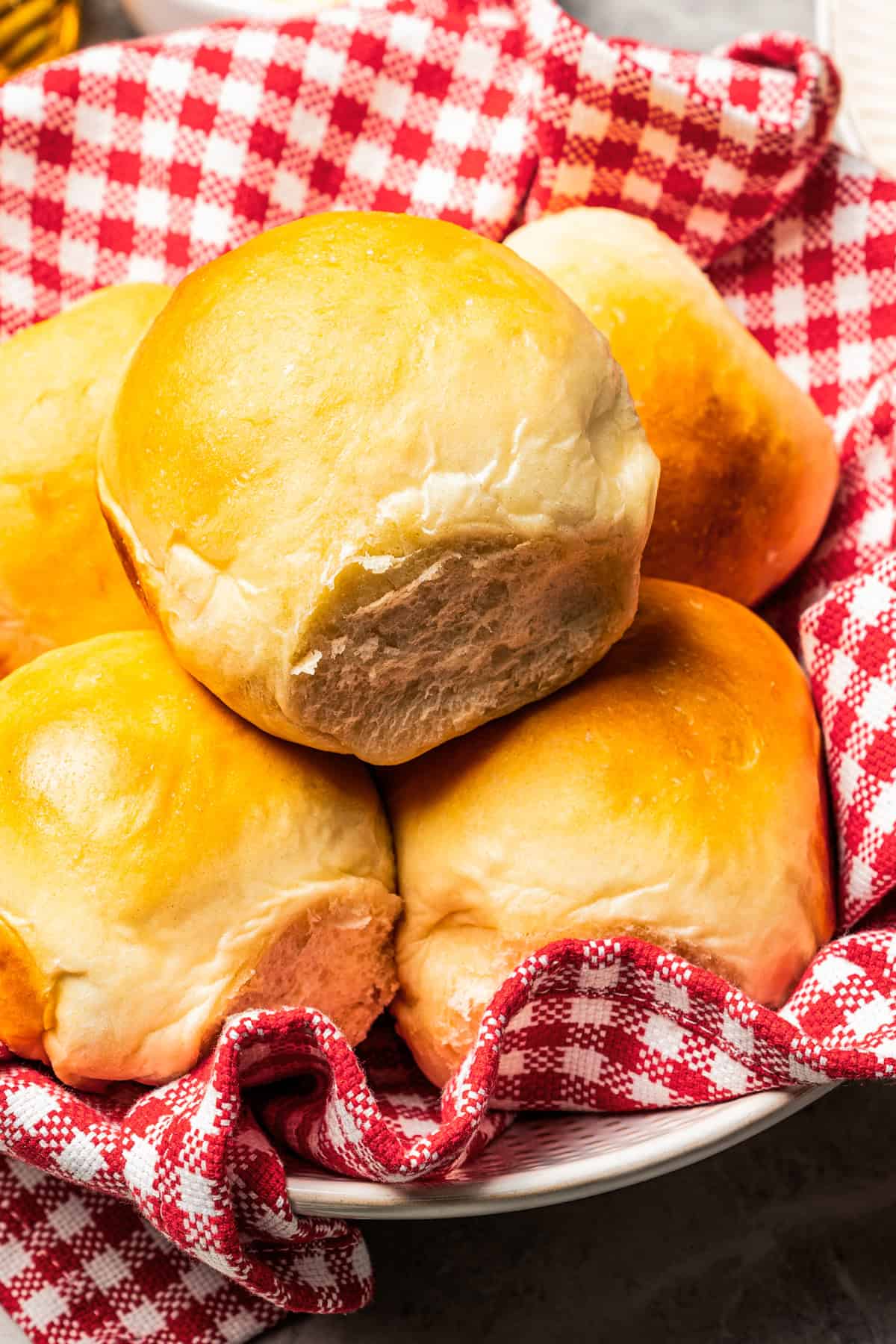 Dinner rolls served in a basket lined with a checkered dishcloth.