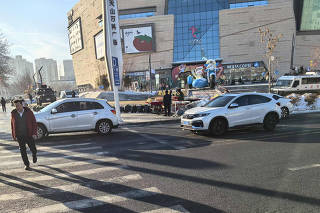 Dois blindados e um carro de polícia guardam a entrada de shopping center em Urumqi, na região autônoma de Xinjiang, no oeste da China, em 15 de dezembro de 2024