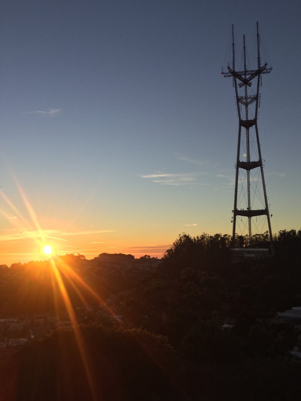 The glowing orange sun barely above the Pacific Ocean on the horizon, Sutro tower a bit closer yet darker, its legs backlit by the setting sun.