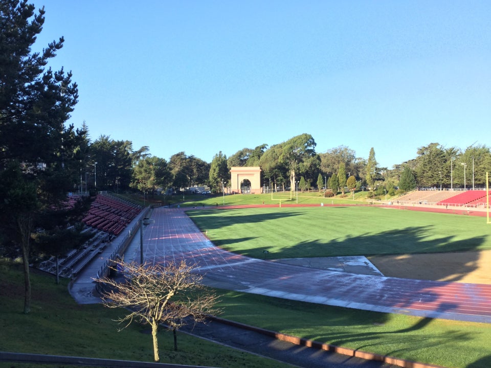 View of Kezar Stadium from the entrance, clear blue sky above, wet track below with almost no runners.