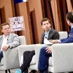 Elon Musk and Sam Altman sitting in chairs next to each other while being questioned by a moderator.