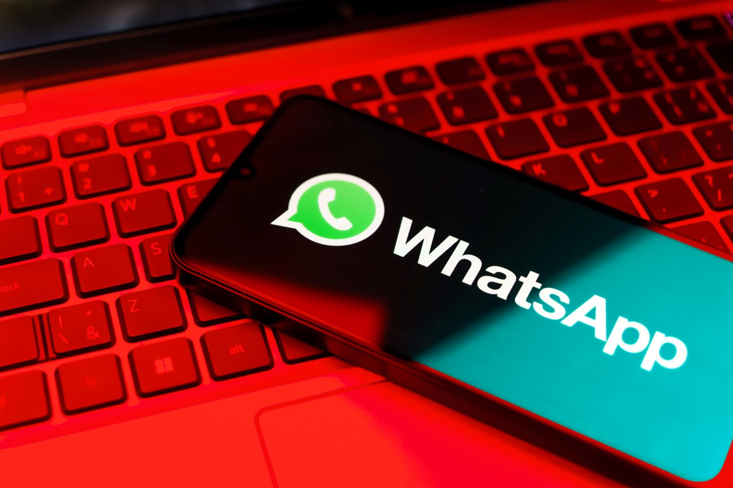 A phone displaying the WhatsApp logo sitting on top of a red keyboard.