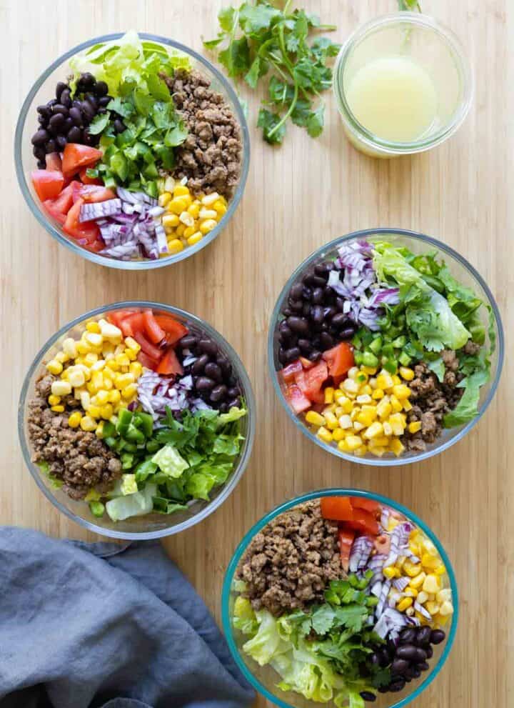 Four Meal Prep Burrito Bowls and a jar with dressing on a kitchen counter.