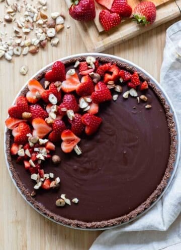 A whole chocolate tart with heart-shaped strawberry pieces on top.