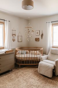 Boho baby room, exuding warm and neutral tones. The centerpiece is a wooden crib adorned withsoft pastel linens and a delicately hanging mobile. A modern, plush glider chair is placed nearby, inviting parents to sit and bond with their little one. A diapering station is thoughtfully arranged on a vintage-style dresser.