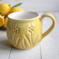 "This pretty mug was hand thrown and trimmed and carved on my pottery wheel using a white stoneware clay. It was bisque fired and glazed with a cheerful yellow glaze on the outside and a matte white glaze on the inside. It was then high fired in my electric kiln. The carvings show a variety of spring flowers with lots of details. This unique cup will compliment any rustic, primitive or minimalist decor. Approximate size: 3.5\" across the top rim and 3.5\" high, holds 14 oz. of liquid. Dishwasher and Microwave Safe. *If this is being sent as a gift please let me know, I'm happy to include a note card with your message the the recipient. Please put your message in the \"note to seller at check out\". To see more mugs and cups please look here: https://www.etsy.com/shop/sheilasart?section_id=