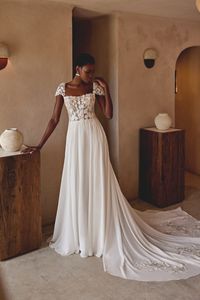 Chiffon A-line gown with straight neckline and detachable cap sleeves. Sheer bodice with exposed boning is adorned with matte floral lace appliques that end at waistline. Buttons to end of zipper. Chiffon skirt billows into a chapel length train with lace cutouts.