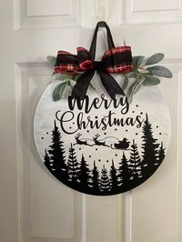 "This Merry Christmas with wooden scenery round door hanger is perfect for way to greet friends and family to your home.  I've embellished this round sign with ribbon and greenery for a statement indoors and out.    Product information:  Dimensions: Approx. 18\"x 1/2\" round  Material: Pine  Finishes: Sherwin Williams Paint, Greenery, ribbon to match. All of DGRKEEPSAKES' signs are created from high quality pine. Each piece is hand cut, sanded, and finished. This will result in slight variations