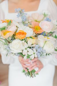 Artfully arranged in a loose and organic style, the colors of yellow, white, peach, and light blue blend seamlessly in this bridal bouquet.