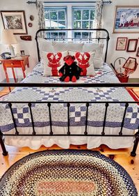 Vintage wrought iron bed with colorful blue quilt with red and white pillows and red stuffed bear.