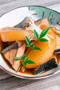 Buri Daikon (Simmered Yellowtail and Daikon Radish) in a small cream bowl with Japanese design topped with decorative leaves