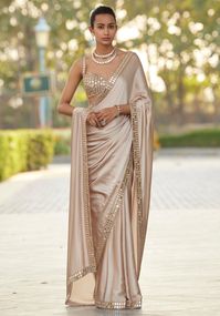 Step into elegance and grace with our beige gold satin saree and mirror blouse set. Crafted from luxurious satin, this saree features a stunning mirror work border enhanced with rose gold embroidery. Paired with a sleeveless blouse adorned with real hand-cut mirror embroidery, this ensemble exudes timeless beauty and sophistication. Embrace the allure of this saree set and make a statement wherever you go. Perfect for Mehendi, sangeet ceremonies, or as a wedding guest, this refined saree set off