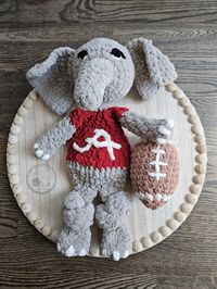 This University of Alabama Big Al inspired elephant snuggle buddy is perfect for your little one to cuddle up with or as an addition to your nursery decor. He would make a great addition to your little one's first football game! * His head is stuffed, but his body remains unstuffed to add to his cuddle factor. His legs are knotted to add texture. * This snuggle buddy is made with high quality, soft blanket yarn. * He measures 16 inches from head to toe - the perfect size for cuddling. * There is an option to add a stuffed crochet football for your snuggle buddy to enjoy! * The eyes, ears, and accents are made of yarn and embroidered on to reduce choking hazards. As with all children's products - please only use with adult supervision. Check your snuggler often for any loose threads that ma