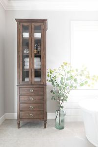 The Restoration Hardware Maison Tall Bath Cabinet, graces a bathroom with a distressed, rustic storage unit.