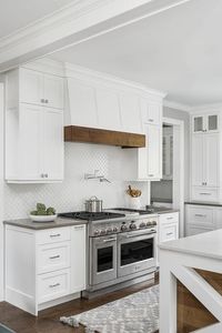 Cottage style range hood features a wood trim above a swing arm pot filler mounted on white arabesque backsplash tiles completing a cooktop design.