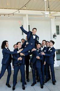 The couple wanted the wedding party to complement the environment of the venue in a timeless and upscale way that reflected the blue lake and beautiful surrounding greenery. The bridesmaids wore dusty blue Azazie dresses with soft, natural glam by LJ Artistry and Reborn Hair Company, and carried bouquets full of soft green, soft pinks, and creams. The groomsmen wore navy blue suits with black lapels and bowties from Men's Wearhouse. #lakewedding #groomsmen