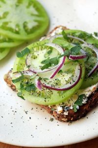 Fall is on the way and our gardens are winding down. Have your tomatoes stopped ripening? Looking for recipes that use green tomatoes? This green tomato toast recipe was a delicious way to use up unripened tomatoes. Make this goat cheese toast with plump green tomatoes, plenty of fresh herbs, and some slivered red onion.