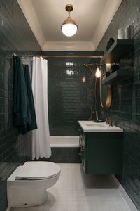 A compact bathroom with dark green subway tiles, a floating vanity, and brass accents, complemented by white fixtures and a shower curtain