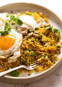 Close up of Curried Rice (basmati rice) with crispy fried egg and a dollop of yogurt on a rustic plate, ready to be eaten