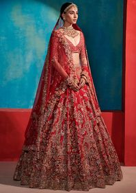 Carmine red raw silk bridal lehenga. Adorned with intricate zardosi and multi colored parsi thread work floral garden motifs all over. Paired with an encrusted choli. Complimented with 2 tulle dupattas – veil and dupatta.