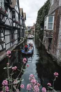 A group of people punting between historic buildings in Canterbury, Kent.