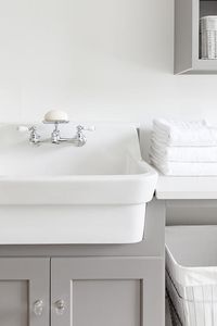 White apron sink and a vintage faucet in a cottage laundry room boasting gray shaker cabinets with glass knobs and white quartz countertops.